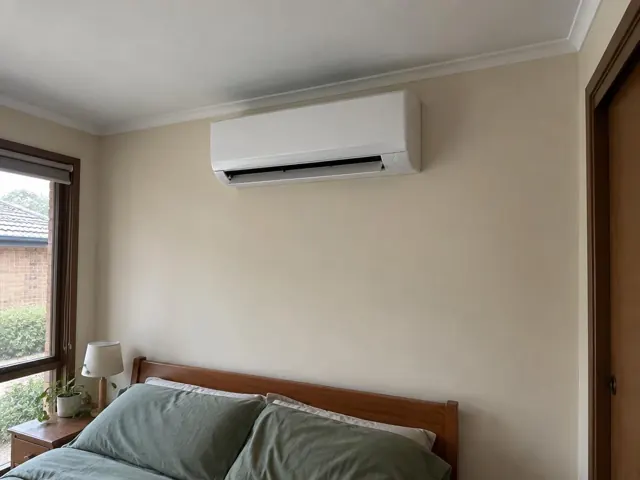 Clean wall-mounted split system above a bed in a beige bedroom in Wynn Vale