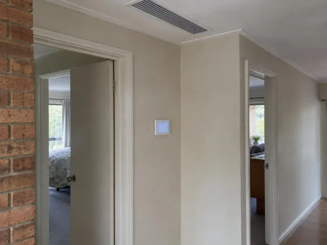 Ceiling ducted air outlet and wall controller in a beige hallway with timber floor in Modbury
